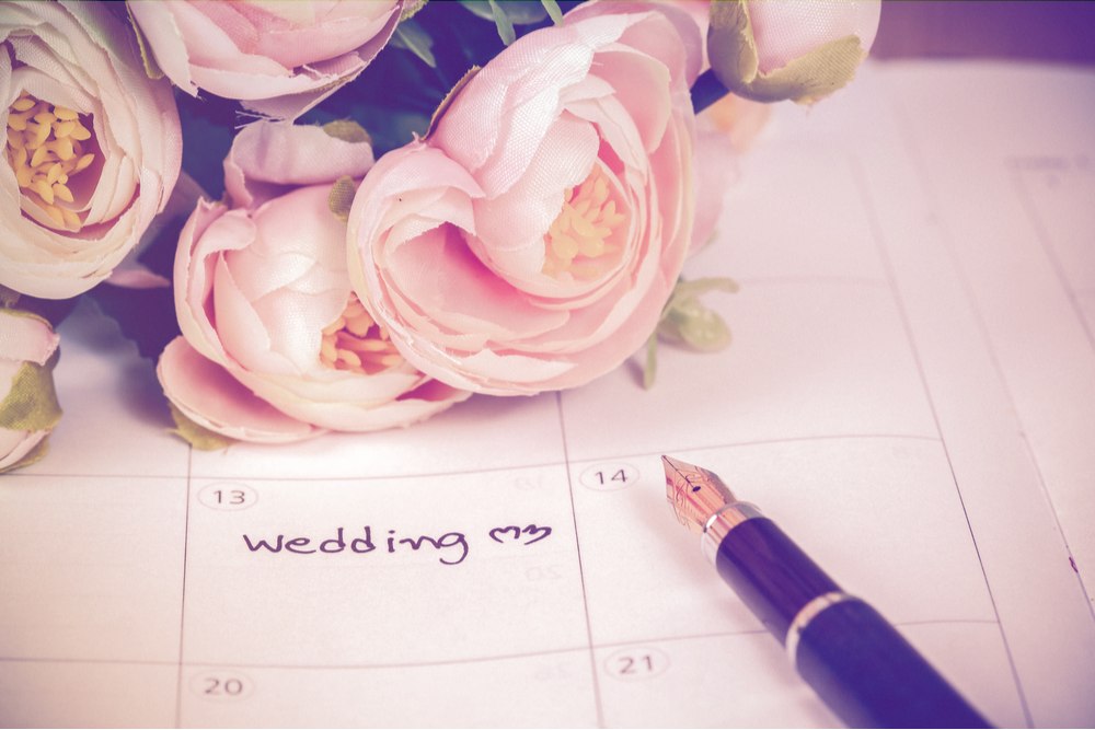 Word wedding on calendar with flowers and pen