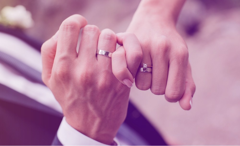 Young married couple holding hands with wedding rings.