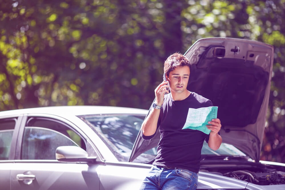 Young man calling for assistance with his car broken down by the roadside