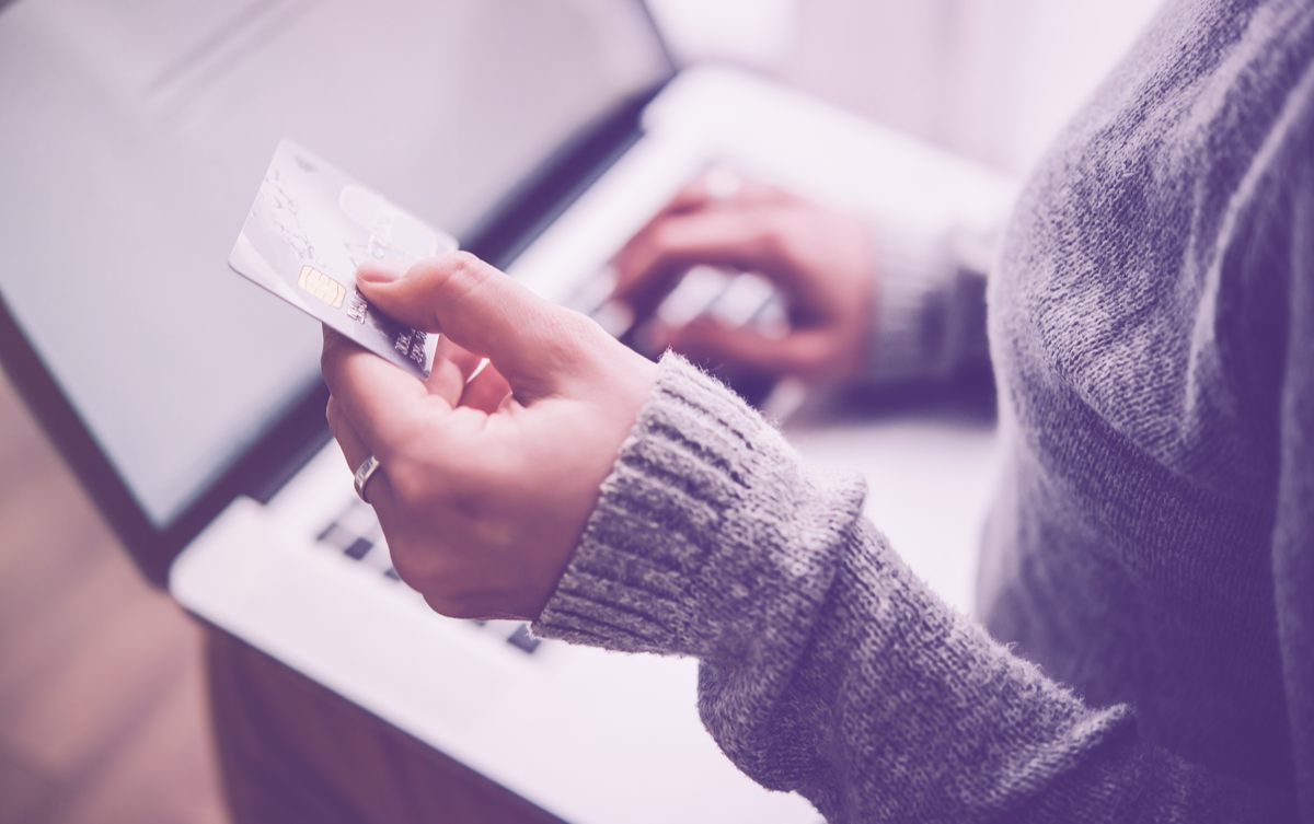 Hands holding plastic credit card and using laptop.