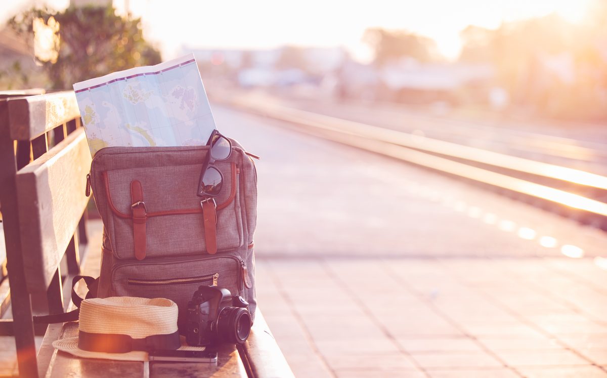 Map in backpack , mobile phone with earphone and hat at the train station.