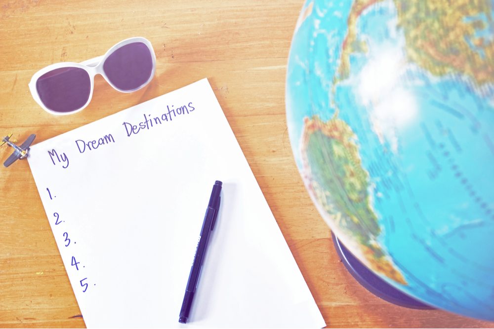 Dream destination list on the paper with pen and world globe map on wooden table.