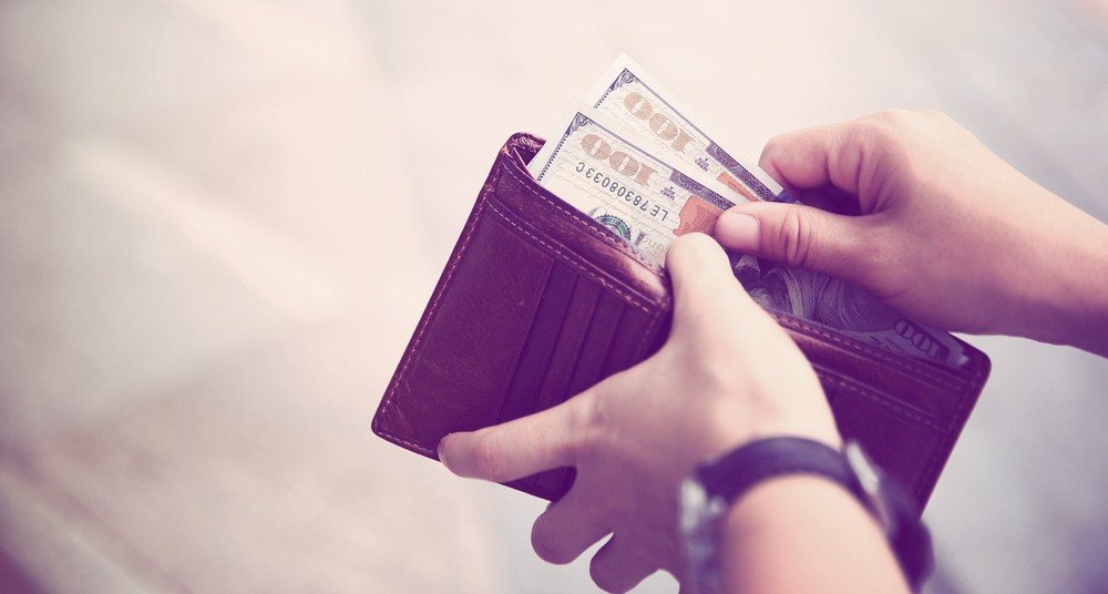 Hands taking out money from wallet on street.