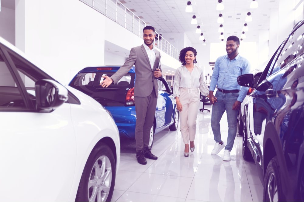 Automobile Seller Showing Luxury Car Consulting Couple Choosing Auto In Dealership Shop.