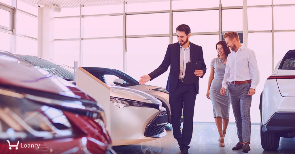Couple and the dealer selling cars look the car in the showroom.