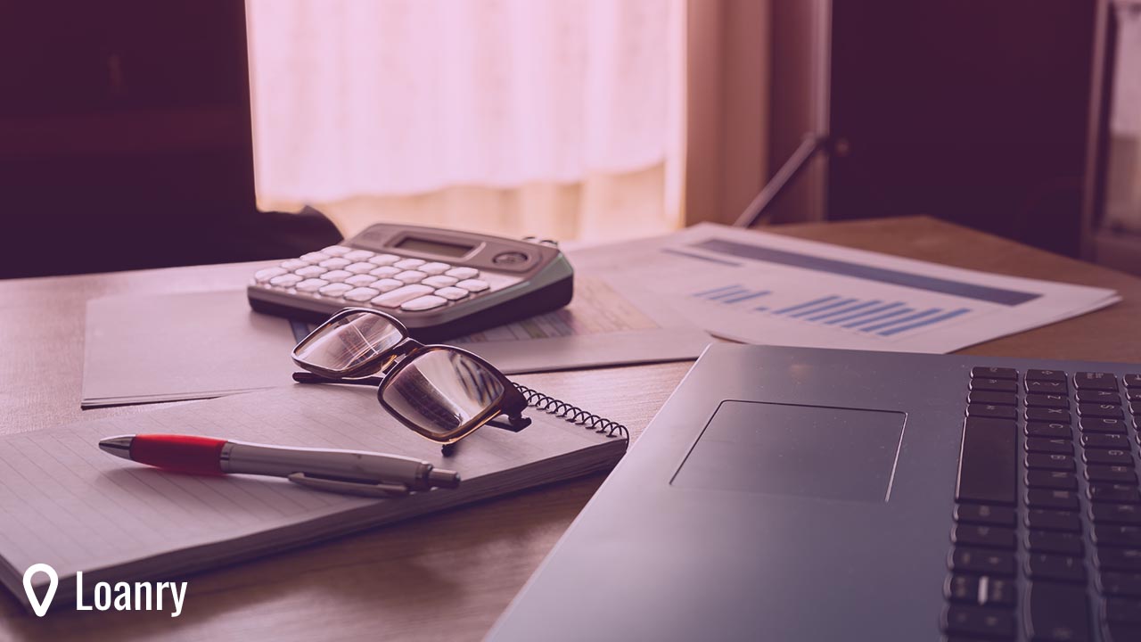 Work table at home with pen, papers, bills, charts, glasses, computer and calculator.