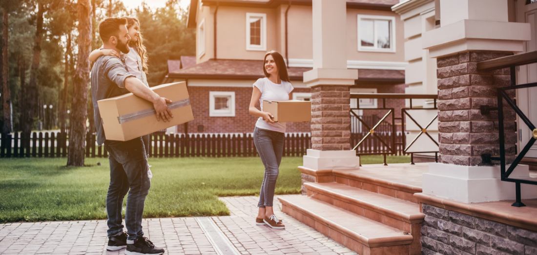 Happy couple is standing near new house with cardboard boxes.